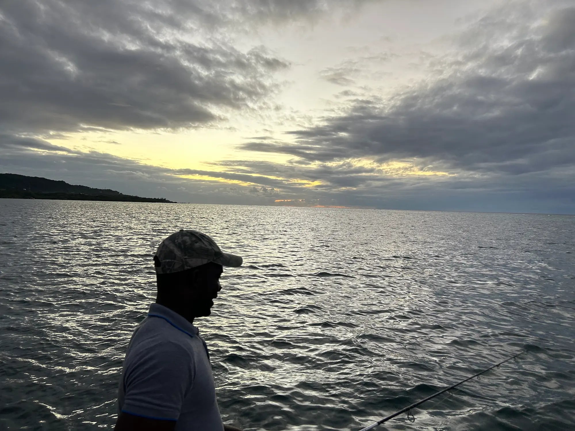 Person fishing on a boat with a cloudy sky and water background
